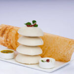 Ghee roast Dosa and Idlii, south indian main breakfast item which is beautifully arranged in a white plate lined with banana leaf and curry as sambar and chutney on white background.