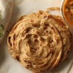 Parotta or Porotta, a layered flatbread made of Maida. This flaky ribbon pancake is a favourite of Kerala. Shot with Butter chicken made of grilled chicken chunks cooked in buttery creamy tomato gravy